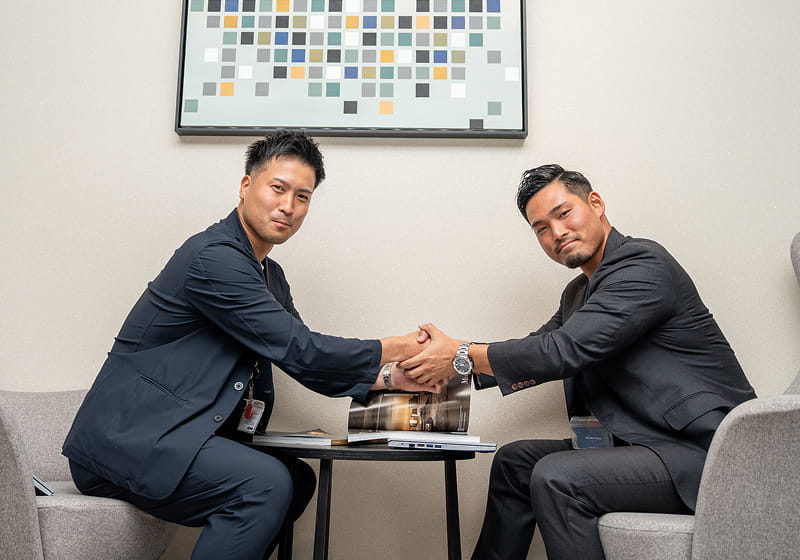 スーツ姿の男性2人がテーブル越しにしっかりと握手を交わしている